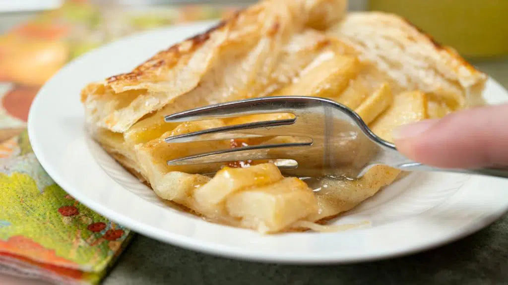 cutting a piece off of a puff pastry apple tart slice