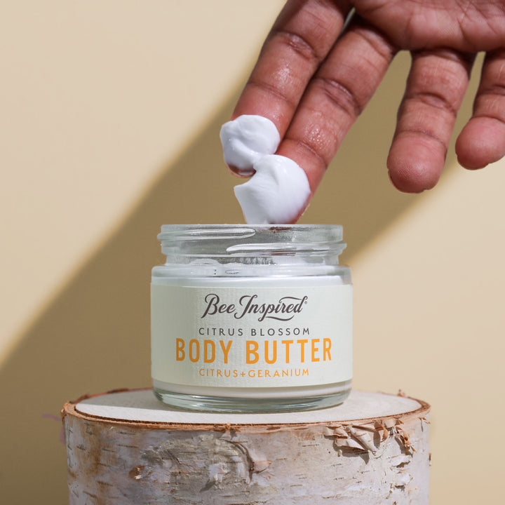 Hand applying body butter to a jar labeled &