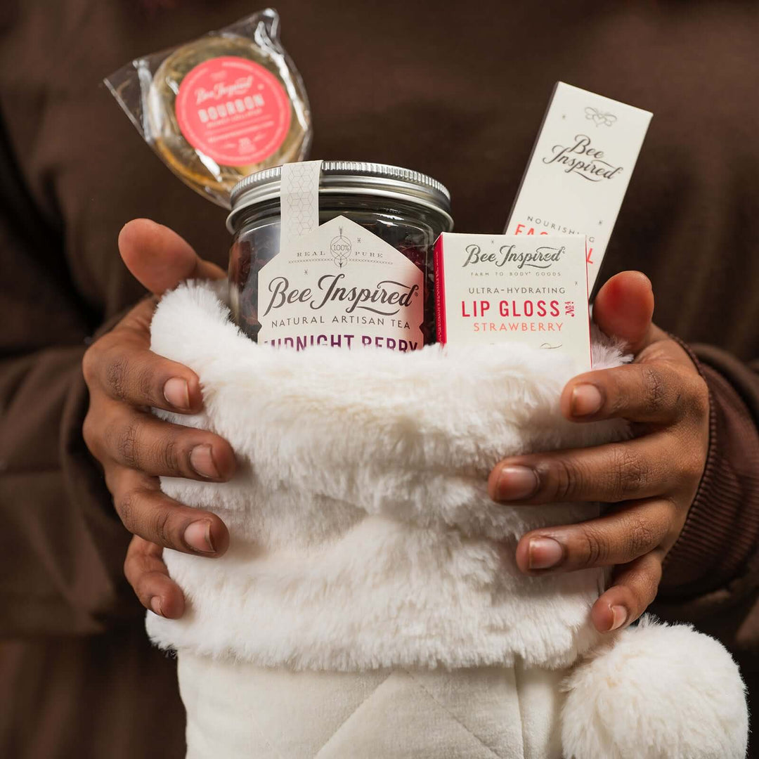 a white fluffy stocking filled with Bee Inspired Midnight Berry tea, strawberry lip gloss, face oil, and bourbon lollipop from bee inspired honey retail store in owings mills
