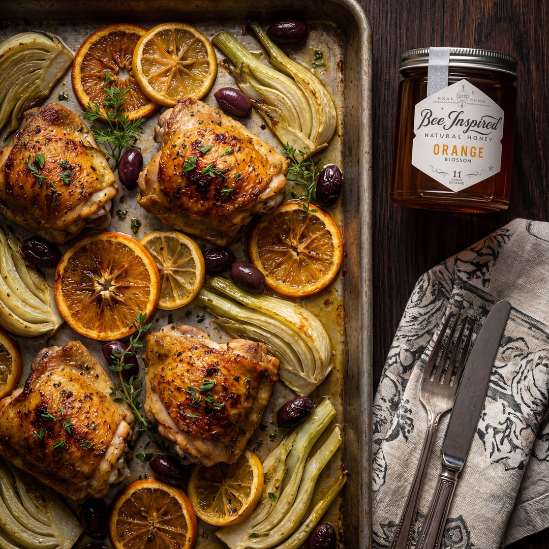 Roasted chicken with oranges and herbs on a baking tray, accompanied by a jar of honey.