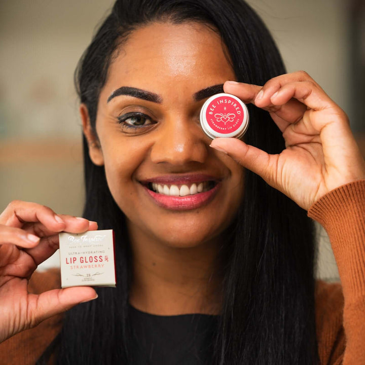 Woman holds strawberry lip gloss in front of her eye as a monocle 