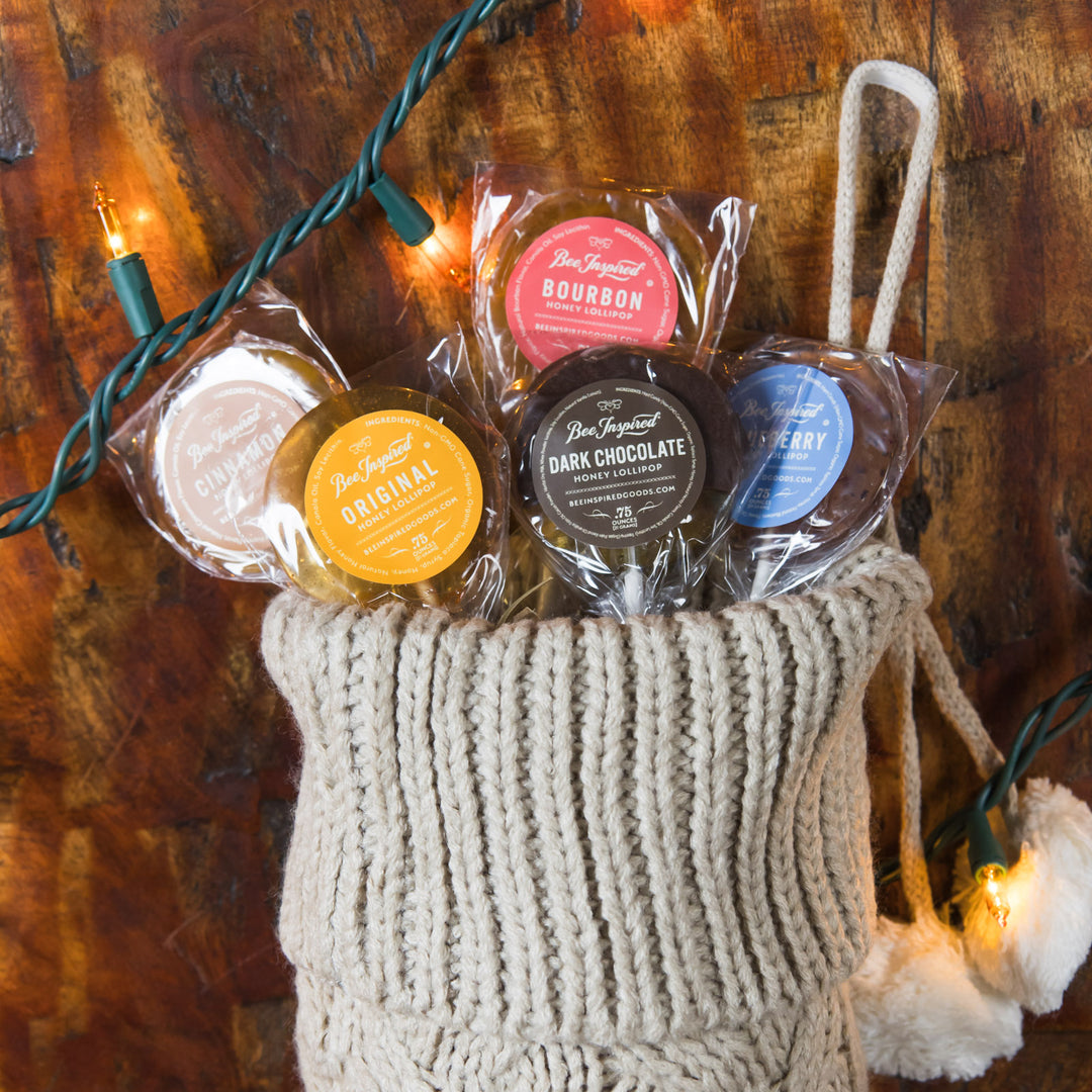 Assorted honey lollipops in clear packaging with colorful labels in a knitted basket on a wooden surface.