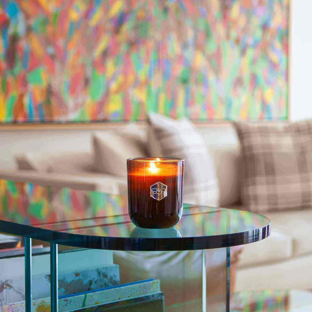 Luxe candle burning on glass table in front of colorful wall 