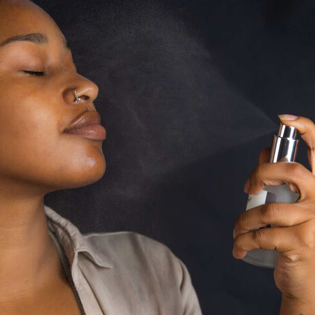 Person using a spray bottle on their face against a dark background
