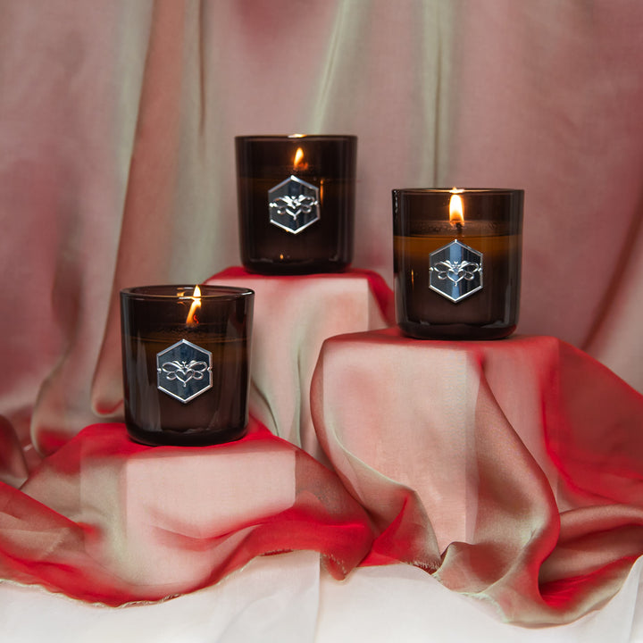 Three black candles with a logo on a pink fabric background