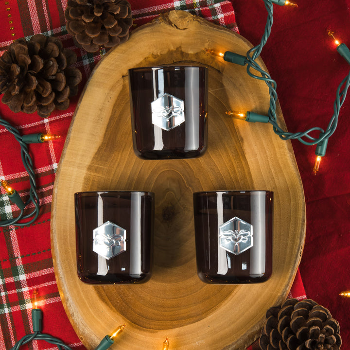 Three dark glass tumblers with a geometric design on a wooden tray, surrounded by Christmas decorations.