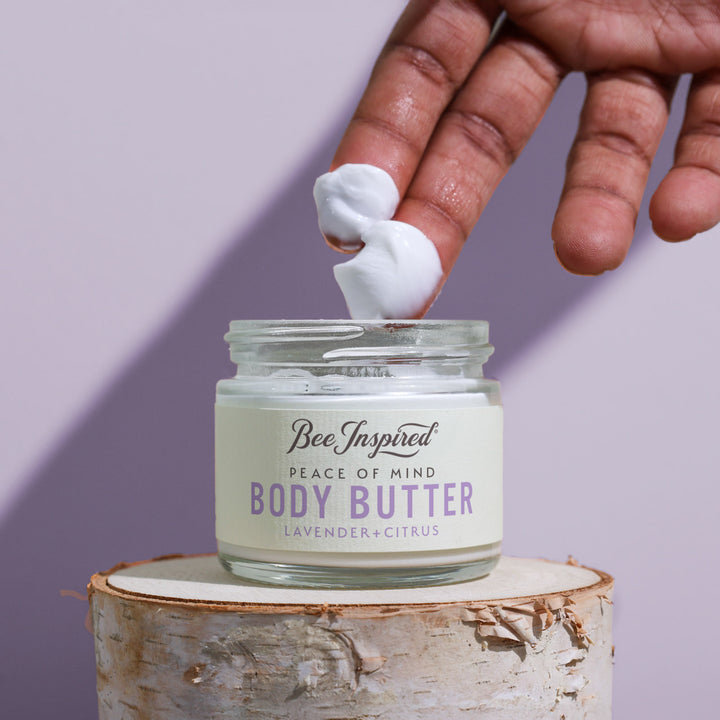 Hand applying body butter to a jar labeled &