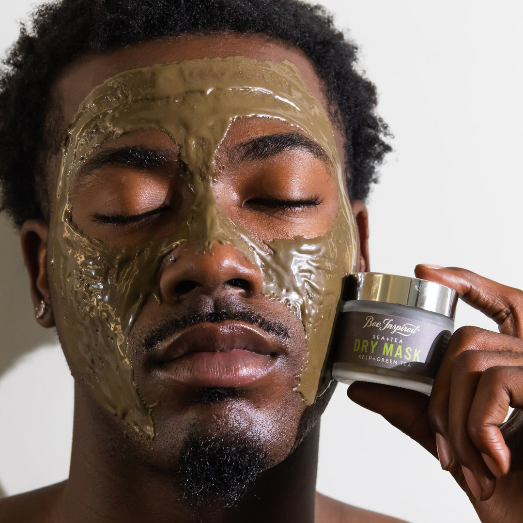 man wearing sea + tea dry mask mixed with honey while holding the sea + tea dry mask container up to his face