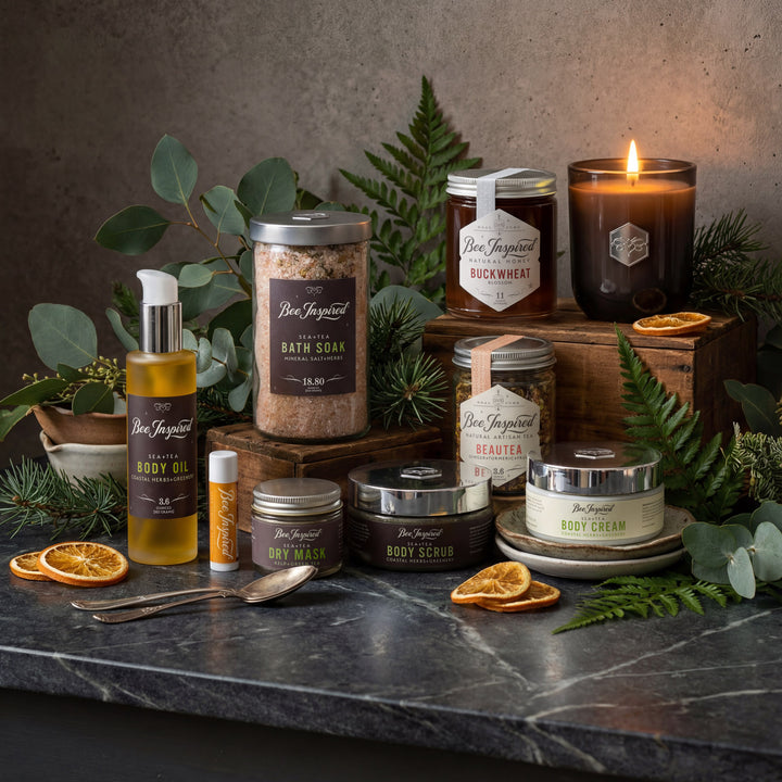 Collection of beauty products including candles, oils, and scrubs on a dark surface with greenery.