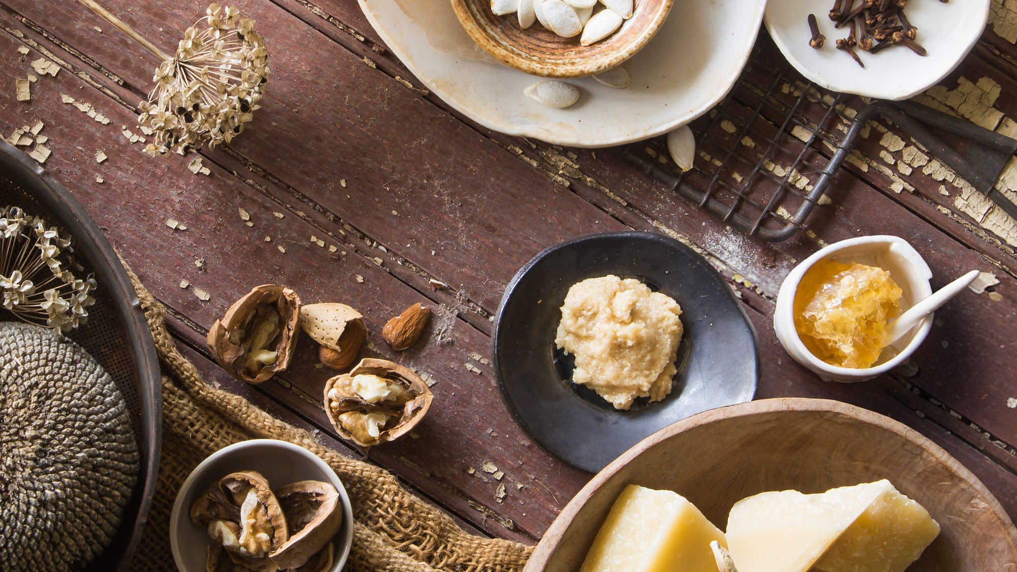 Assorted ingredients on a wooden surface, including nuts, seeds, and a bowl of butter.