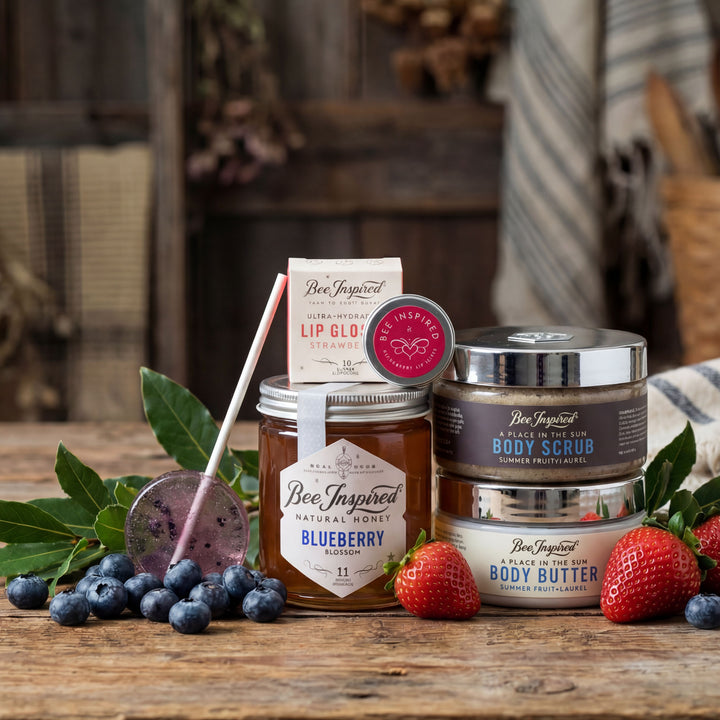 Bee-Inspired natural beauty products including honey, lip gloss, and body scrub on a wooden surface with berries and leaves.