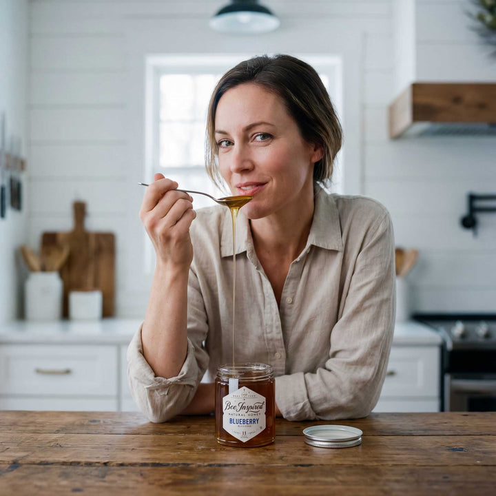 Woman in a kitchen pouring honey from a jar with a spoon.