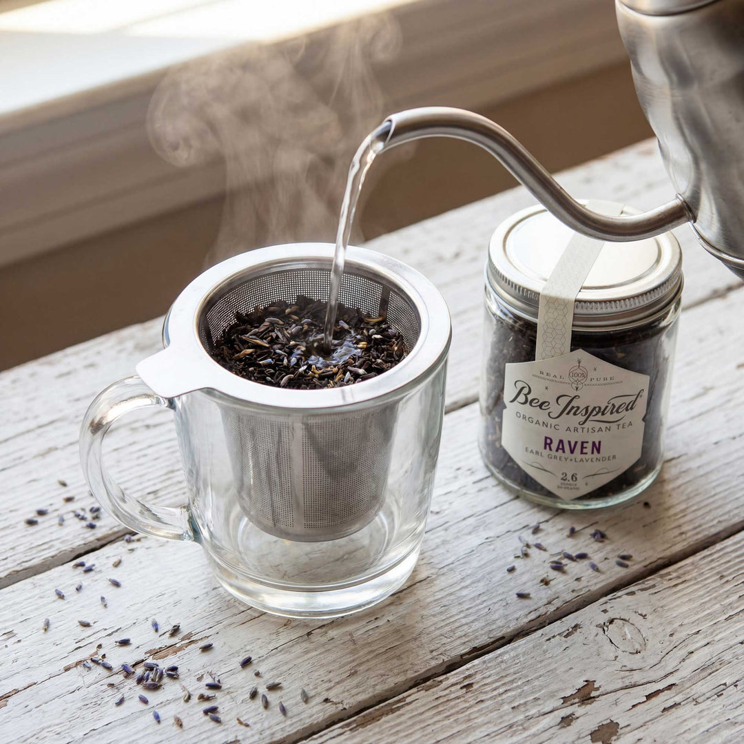 Tea being poured into a glass mug with a tea strainer, next to a jar of &