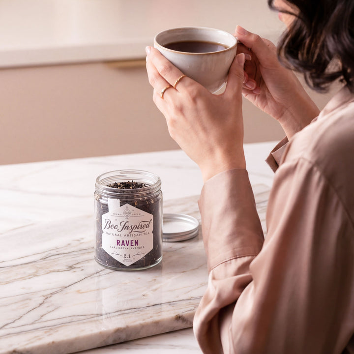Person holding a cup of raven tea with a tea jar labeled &