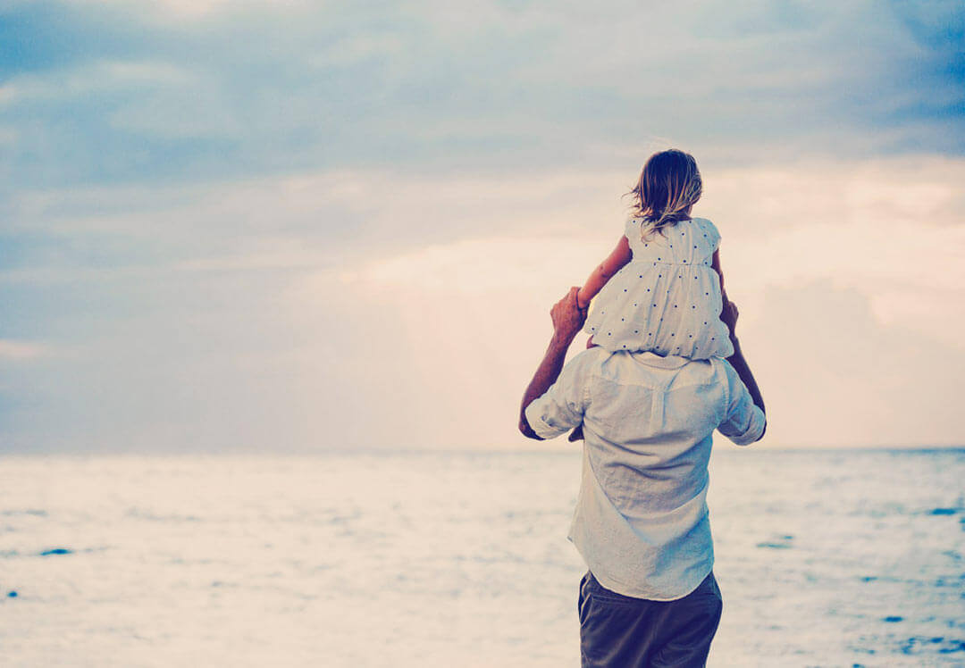 girl sits on her father's shoulders at the beach