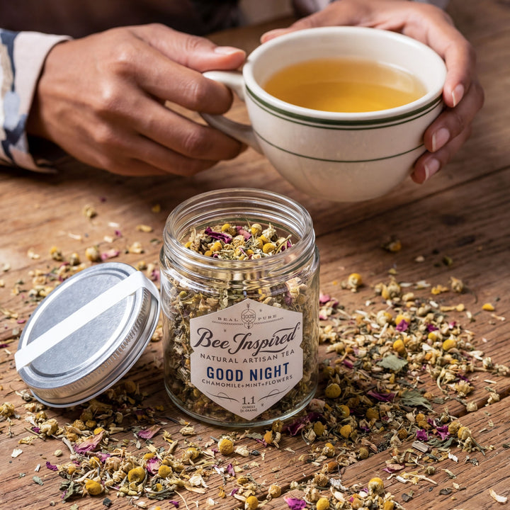 Person holding a cup of tea with a jar of &