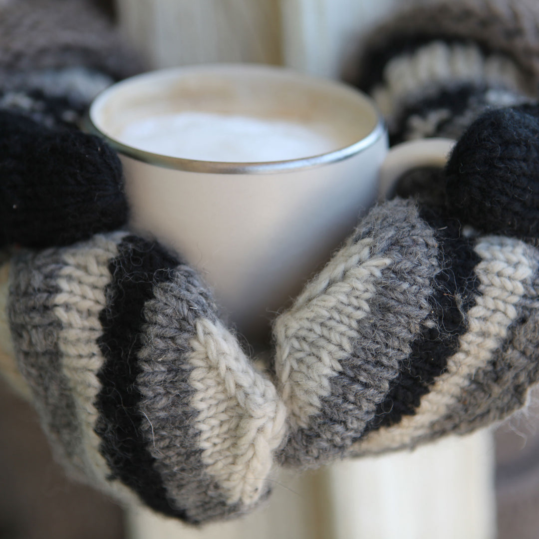 Pair of hands wearing striped mittens holding a cup of coffee.