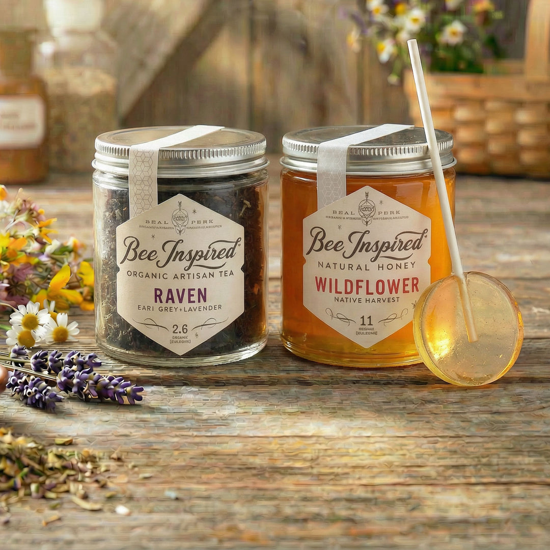 Two jars of 'Bee Inspired' tea and honey on a wooden surface with flowers and a spoon.