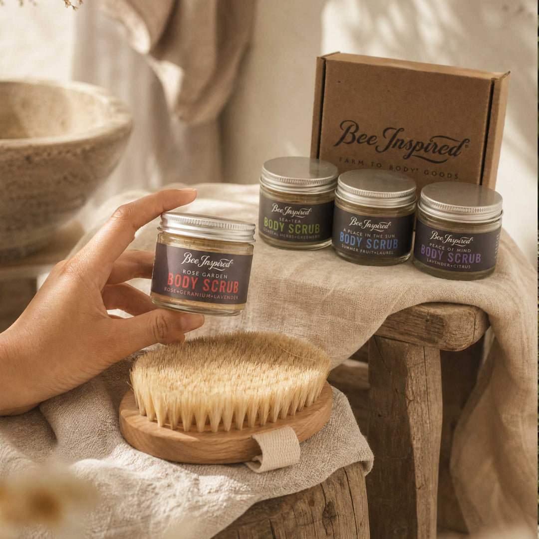 Bee Inspired body scrub jars with a brush and packaging on a rustic wooden table.