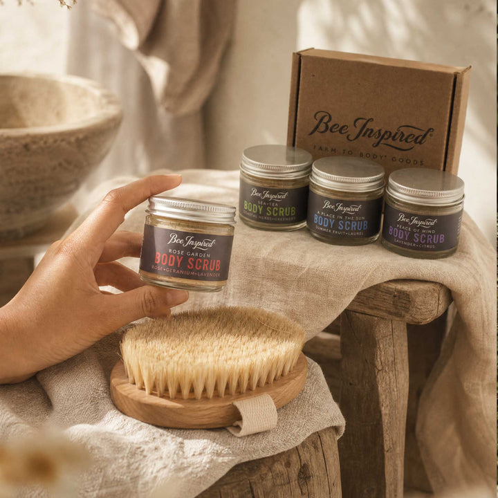 Bee Inspired body scrub jars with a brush and packaging on a rustic wooden table.