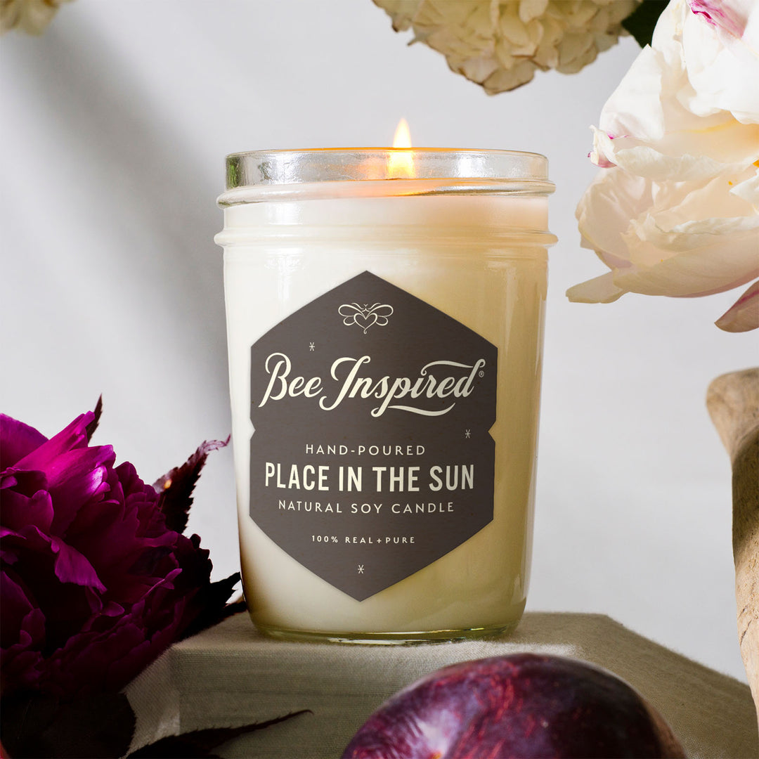 Place in the Sun jelly jar candle burning next to white and purple flowers 
